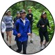 A group of women jogging on a gravel path surrounded by lush greenery. They are wearing athletic clothing and hats, appearing energetic and joyful.