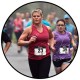 A group of runners participating in a race. The focus is on a woman in a red tank top wearing earphones and bib number 23, running alongside others in the event. The background is slightly blurred, emphasizing the movement and energy of the scene.